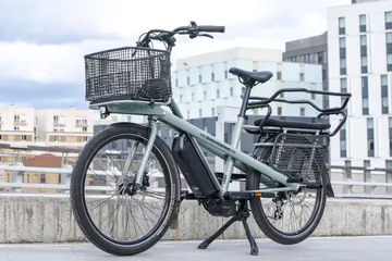 Sage-green long-tail electric cargo bike with a padded rear child deck and front basket