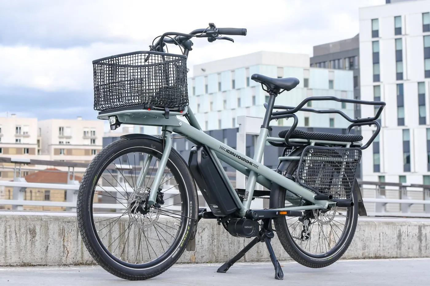 Sage-green long-tail electric cargo bike with a padded rear child deck and front basket