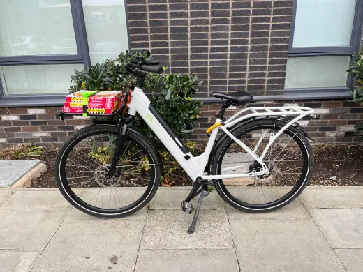 Pizza boxes strapped to the front rack of a CYCL e-bike outside a brick building