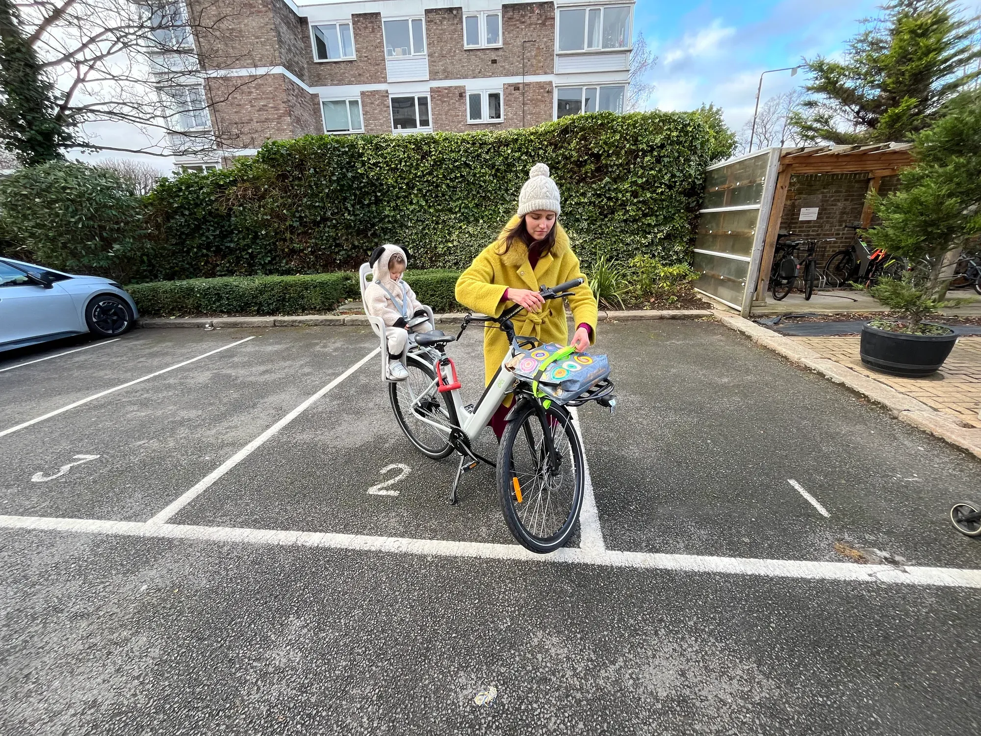 Mum loading a bag onto the front rack of a CYCL compact e-bike while her toddler sits in the child seat