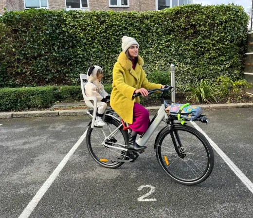Mum riding the CYCL compact e-bike with her toddler in the child seat and a bag on the front rack