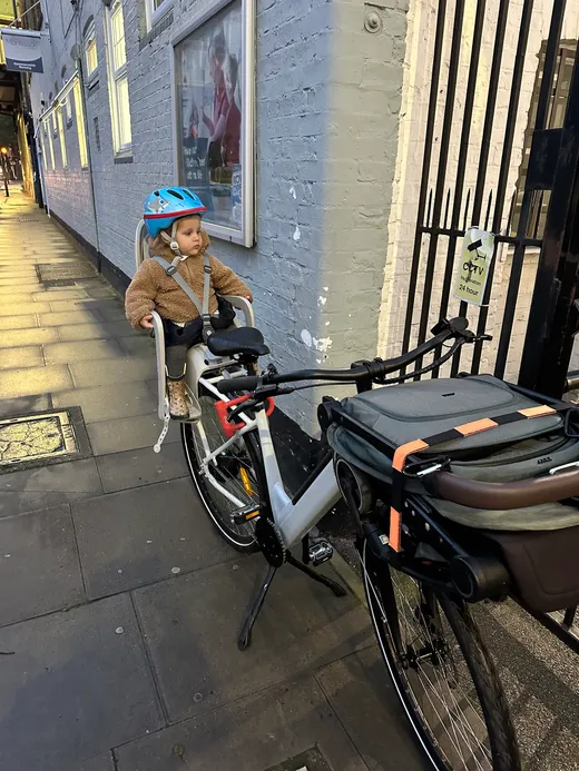 Toddler in a blue helmet waiting in the child seat on a London street